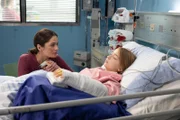 Lisa (Martha Haberland, r.) liegt in ihrem Bett und schläft noch die Narkose aus. Henriette (Anna Puck) ist bei Ihr.