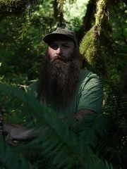 Matthew Raney in green t-shirt in forest holding his gun.
