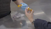 Zwei CBP-Beamte halten in Calexico, Kalifornien, medizinische Tablettenfläschchen, die in den Habseligkeiten eines Passagiers in ihrem Fahrzeug entdeckt wurden (National Geographic for Disney).