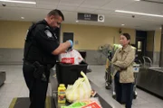Officer Graham untersucht weiterhin die Lebensmittel aus der Transportkiste der Familie. (National Geographic/Lucky 8 TV)