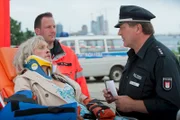 Hans (Bruno F. Apitz, r.) versucht die verletzte Eva Dorint (April Hailer, l.) zu befragen, doch die bekommt infolge ihrer Verletzungen nicht einmal ihren Namen heraus. (im Hintergrund Komparse).