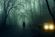 Ein Horror-Konzept. Ein Mann, der neben einem Auto steht und ein Monster mit glühenden Augen betrachtet. In einem gespenstischen, nächtlichen Winterwald Mit einer Grunge-Texturbearbeitung