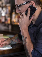 portrait of pub/bar owner working on smartphone and electronic tablet at bar drinking coffee