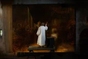 Rembrandt steht auf einer Bank und malt ein grosses Bild.