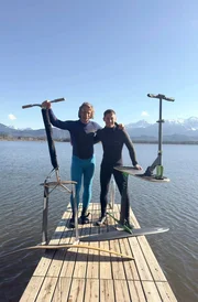 Erfinder Jan Grebe (links) am Hopfensee im Ostallgäu. Er hält in seiner Hand das von ihm entwickelte Wassersportgerät. Neben ihm steht Foil Boarding-Influencer Valentin Hiermeier. Auch er hat eine Foilboard-Variante in der Hand.