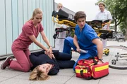 Die Angst-Patientin Birgit Paschke (Winnie Böwe, M.v.) wollte vor ihrer OP fliehen. Vor der Klinik bricht sie zusammen. Julia Berger (Mirka Pigulla, l.) und Ben Ahlbeck (Philipp Danne, r. mit Komparsen, h.) kümmern sich um sie.