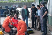 Während Dr. Haase (Fabian Harloff, l.) sich um den verletzten Taucher kümmert, befragen Melanie (Sanna Englund, 4.v.r.) und Mattes (Matthias Schloo, r.) seine Kollegen Werner Grün (Manfred Zapatka, M.), Razoul (Orazio Zambelletti, 3.v.r.) und Heiko Sammer (Rudolf Schwarz, 2.v.r.).