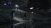 Detectives stand near the water's edge.