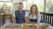 Peter und Isabelle Kleber von der Schatzbergalm über dem Ammersee sitzen an einem Tisch auf der Terrasse und präsentieren verschiedene Gerichte.