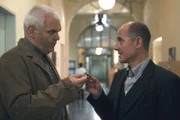 Dr. Robert Kolmaar (Ulrich Mühe, r.) wird von dem Schweizer Peter Lawin (Lázló I. Kish, l.) gebeten, dem toten Herbert Jank ein Amulett beizulegen.