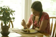 A young girl sits at a dining table with a plate of food.