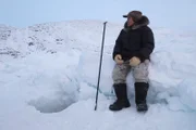 Lukasi Naappaluk waits by a hole dug out of the ice - he hopes to find some mussels for the Inuk to use to supplement their diet.