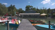 Blick auf das Seehaus Raabe am Wörthsee. Im Vordergrund stehen bunte Boote an einem Bootssteg.