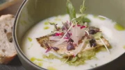 Im Seehaus Raabe am Wörthsee wird als Vorspeise Renkenfilet lauwarm gebraten in Buttermilch auf Avocadocreme mit Radieschen, Bio-Holundersirup und selbstgemachtem Schnittlauchöl in einer Suppenschüssel präsentiert mit einer Weißbrotscheibe als Beilage.