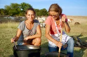 Mirabella (li.) und Elena Migit (re.) bereiten auf dem offenen Feld einen Lammeintopf zu.