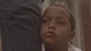 Young Demery's face leans against a grown-up leg.