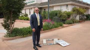 Host Anthony Melchiorri stands next to a broken sign outside the Posada de San Juan in San Juan Bautista, California.