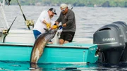Johnathan Hillstrand and Casey McManus pulling on a fishing rod. Our field producer Bryan Miller filming