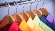 Rainbow colored shirts on hangers.