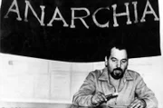 Der italienische anarchistische Aktivist Giuseppe Pinelli in den 60er Jahren: hinter ihm eine Flagge, auf der „Anarchie“ steht