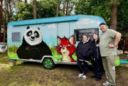 Jasmin, Alina und Sven Ruby vor ihrem bunten Wohnwagen.