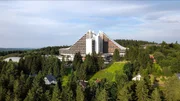 In der der DDR wurde gleich mit ihrer Gründung der Bau von Ferienkomplexen zur Pflicht, schrieb doch die Verfassung das Recht jeden Bürgers auf Urlaub fest. Das ehemals der Oberschicht vorbehaltene Privileg des Reisens durfte zu einem Volkssport werden. Dabei entstanden riesige Freizeitmaschinerien, die unter Verwendung moderner Baumaterialien eigene Architekturtypen generierten. So mischen sich in die Urlaubsarchitektur der ersten Jahrzehnte regional-nationale Traditionen mit sowjetisch-sozialistischem Klassizismus und der Klassischen Moderne. Mit der Ausweitung der Bauprogramme in den 60er Jahren erfolgte die Typisierung, die mit Modulen des allgemeinen Wohnungsbaus operierte. Dieser Linie folgend entstanden auf Rügen Urlaubssiedlungen, Visionen vom "sozialistischen Seebad", die mit den Ferienzentren der großen europäischen Strände mithalten sollten. Für den Gebirgs- und Wintersporturlaub verwandelte man den thüringischen Gebirgsort Oberhof in ein neues "sozialistisches St. Moritz". Hier entstanden repräsentative Interhotels und Ferienheime mit ehrgeiziger Architektur: So wurde die Bergtopographie durch abgetreppte und abgeschrägte Baukörper verlängert, die Ästhetik der Landschaft mit Bergspitzenmotiven und Dreiecksmotiven weitergeschrieben, unter Verwendung von vorwiegend Beton, aber auch regionalen Materialien wie Naturstein, Schiefer und Holz. Der Film "Urlaubsträume in Beton: DDR" wirft einen prüfenden Blick zurück auf die architekturästhetische und soziologische "Haltbarkeit" des damals Gebauten.