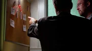 Zwei Kriminalbeamte untersuchen eine Tafel mit den gesammelten Daten zu diesem Fall.