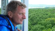 Für seine neue Expedition geht Michael Kessler buchstäblich an die Grenze. Rund 1.400 Kilometer legt der Comedian im Tuk Tuk zurück. Mit dem ostasiatischen Dreirad fährt er von Bayern bis an die Ostsee, immer entlang des ehemaligen deutsch-deutschen Grenzstreifens, um zu erfahren, ob 25 Jahre nach dem Mauerfall auch wirklich zusammen gewachsen ist, was zusammengehört. Der erste Teil der Expedition führt ihn vom alten Grenzstein im Dreiländereck nahe Hof zwischen Bayern, Sachsen und Tschechien bis nach Bad Sachsa im Harz. - Michael Kessler schaut vom Bayernturm auf das grüne Band. Der Turm steht auf dem unterfränkischen Büchelberg im Naturpark Haßberge, zwischen Zimmerau und Sternberg im Grabfeld, direkt an der Grenze zum Freistaat Thüringen.