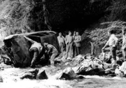 Die Untersuchung des Wagens des Pressefotografen Lansky, den man fünf Kilometer vor der österreichischen Grenze zertrümmert und ausgebrannt in einer Bergschlucht gefunden hat. In der Gruppe am Ufer von links: Brettschneider (Willy Harlander), Lenz (Helmut Fischer) und Veigl (Gustl Bayrhammer).