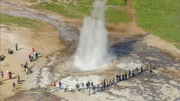 Die sprudelnden Geysire sind eine der Hauptattraktionen für Inselbesucher. Eine Wasserfontäne schießt in die Luft, drumherum stehen Menschen.