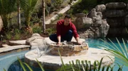 Wide Shot of Brian standing on fireplace table inside of pool installing net to fire pit, as seen on Pool kings.