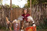 Checker Tobi in Legionärsausrüstung vor einem Castrum.