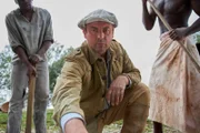 Ausschnitt Spielszene: Der Ingenieur Bernhard Sattler (Eckhard Preuﬂ, M.) bekommt von afrikanischen Helfern gewaltige, versteinerte Knochen gezeigt. Nicht der erhoffte Bodenschatz, doch der Beginn einer der erfolgreichsten Expeditionen in der Geschichte der Paläontologie.