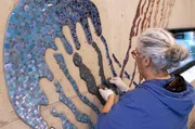 Tanja Lebski verfugt und finalisiert das Mosaikkunstwerk für das Hallenbad einer Schule.