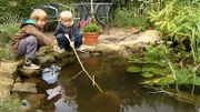 Bennet und Levin fischen mit einem Käscher im Gartenteich nach Wasserläufern und Fröschen.