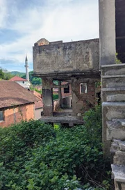 Ein im Krieg zerstörtes Haus, im Hintergrund die weiße Moschee von Srebrenica