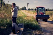 Während Julian (Ben Münchow) am Feldrand pinkelt und telefoniert, hat er seine Tasche gefährlich nah an der Straße abgelegt. Ob der ominöse, sich nähernde Traktor da einfach vorbeifahren kann?