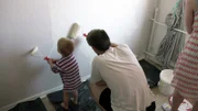 Papa Maik und Sohn Lennox streichen gemeinsam die Wand.