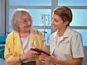 Auch Verena Stehle (Dorothea Walde, li.) muss mit Herzproblemen für weitere Untersuchungen in der Sachsenklinik bleiben. Sie macht sich allerdings Sorgen um ihre Hündin Lara, deren Foto sie Schwester Arzu (Arzu Bazman, re.) zeigt. Nach kurzer Überlegung bietet Arzu Verena an, sich während ihres Klinikaufenthaltes um Lara zu kümmern.