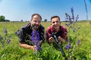 Naturfilmer Jan Haft (l.) nd Eric Mayer (r.) liegen in einer Wiese. Eric Mayer hält eine Kamera mit Schnorcheloptik in Händen.