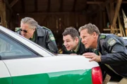 Hubert (Christian Tramitz, rechts), Riedl (Paul Sedlmeir, Mitte) und Girwidz (Michael Brandner) gehen in Deckung. Lässt Bauer Meißner tatsächlich die Scheune in die Luft gehen?