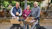 Björn Freitag (l) mit Michael Ullenbruch (r) und Jennifer Schneider vom Klostergut Laach. In Björn Freitags Fahrradkorb landen Eisbein, Schweinenacken und Hanföl vom Klostergut sowie Aal aus dem Laacher See.