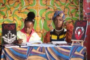 Bisma (Faith Omole, r.) träumt davon, dass "Lady Parts" internationale Berühmtheit erlangt – und sie und ihre Tochter Imani (Okpenerho Edesiri, l.) dadurch dem Leben am Comic-Stand auf dem Markt entkommen könnten.