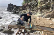Ein Goldtaucher am Strand bei Pinut-An siebt Sand aus Säcken: Das darin enthaltene Gold bleibt an der Matte hängen.