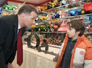 Roland Heilmann (Thomas Rühmann, li.) ist mit seinem Enkel Jonas (Anthony Petrifke, re.) im Spielzeugladen und hat alle Hände voll zu tun, ihm eine teure Autorennbahn auszureden.