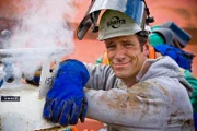 Portrait of Mike Rowe next to venting gas on torch bottles. Notice sticker "Pressure Building".