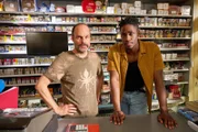 Paul (Ben Andrews Rumler, r.) arbeitet im Kiosk seines Chefs (Matthias Thönnissen, l.). Ob der ihm einen Vorschuss gewährt, damit er seiner Familie Geld für eine neue Wasserpumpe schicken kann?