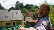 Josef Epp allein auf der Gartenbank hinter seinem Haus. Im Hintergrund: Blick auf Bad Grönebach.