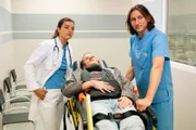 Kurz vor seinem Tod wurde Marten Keller (Cedric Sprick-Benz, M.) ins Krankenhaus eingeliefert, da seine Hand nach einer Straßenblockade nicht mehr vom Asphalt zu lösen war. Laut der behandelnden Ärztin Dr. Diniz Aslan (Altine Emini, l.) und Pfleger Alex Marbacher (Liliom Lewald, r.) wies der Körper des Klimaaktivisten noch weitere Verletzungen auf.