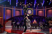 Moderator Kai Pflaume (M.), Rateteam-Kapitän Elton (r.) und das Publikum, sind beeindruckt von der Darbietung der Akrobat:innen Merrylu und René Casselly.
